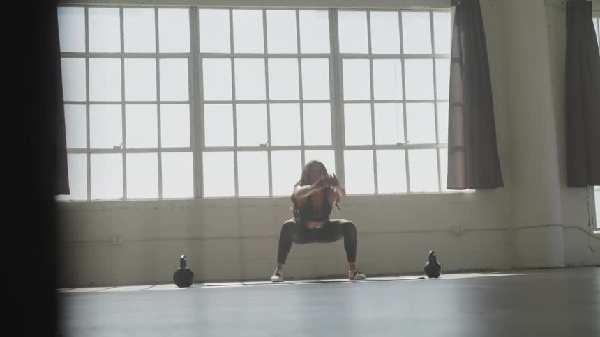 Female with long hair doing squats and lunges in front of a large window