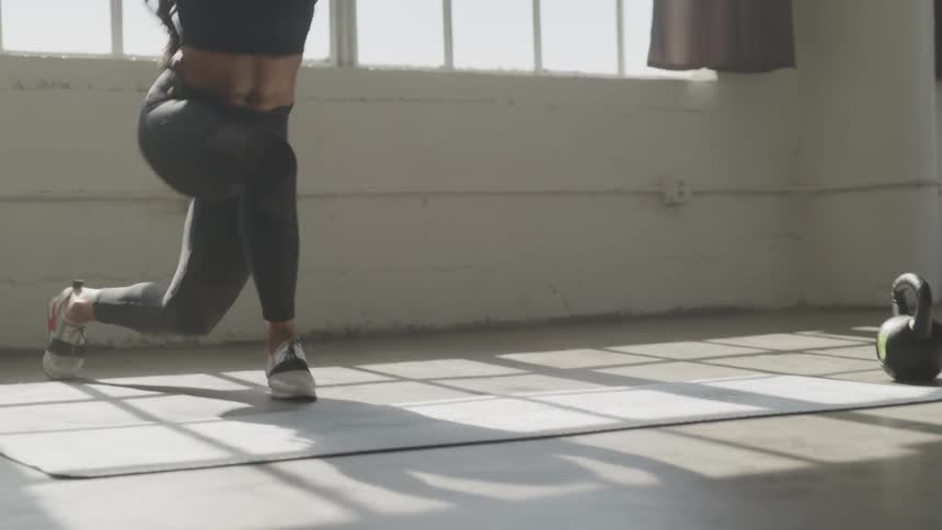 A woman holds her arms out in front of her as she does squats and lunges near a large window