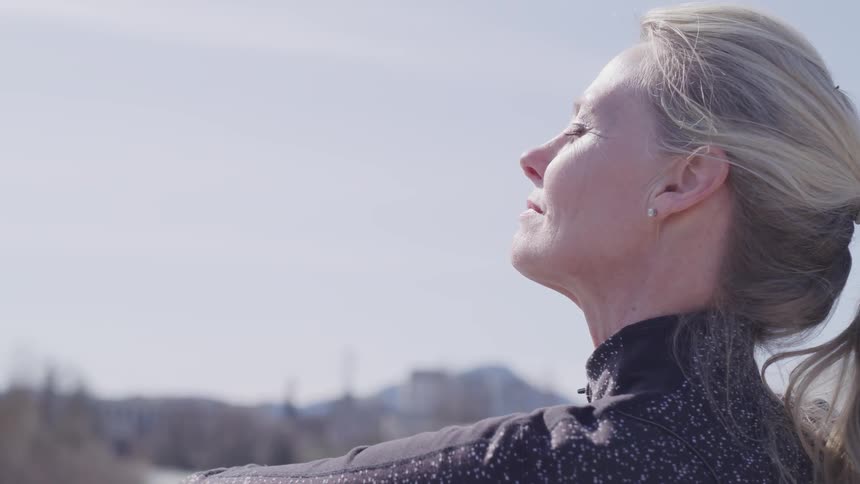 A woman stands with her face up towards the sun