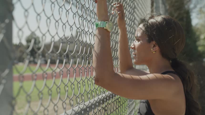 A woman looks at a baseball diamond through a chain link fence
