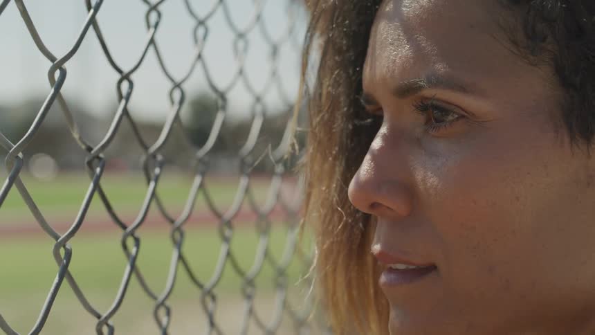 A woman looks through a chain link fence at a track field