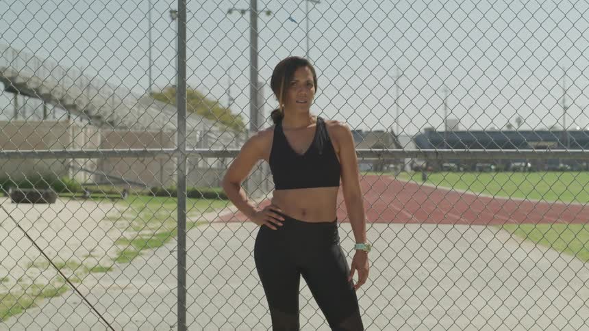 A woman in workout clothes stands by a fence and poses