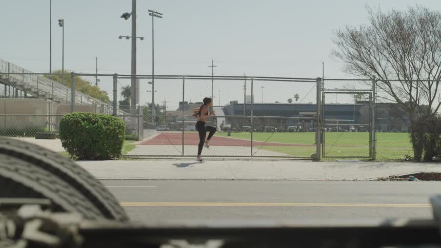 Woman warms up and starts running on the pavement next to the wire fence during daylight