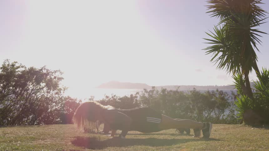 Two women do push ups in the grass near the water