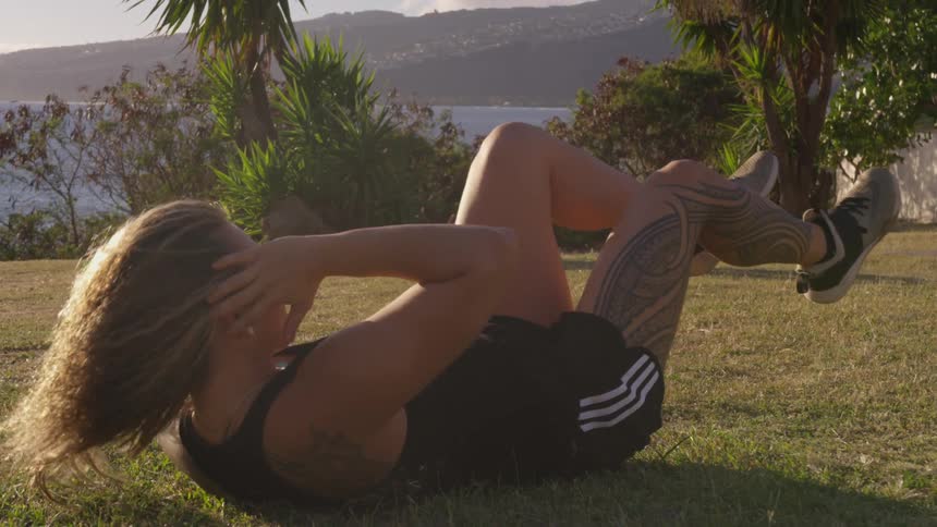 Woman does crunches laying in grass near ocean