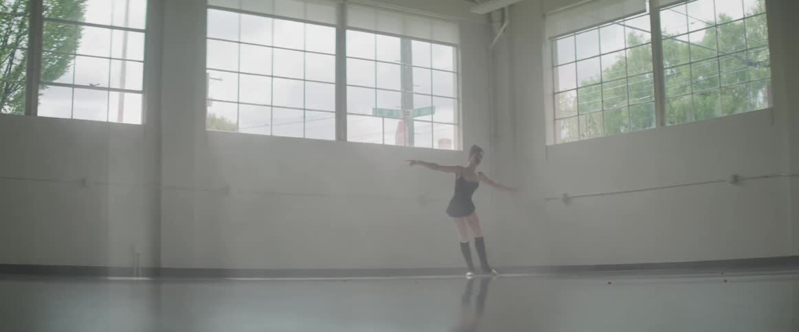 A woman dancing in a well lit studio with large windows