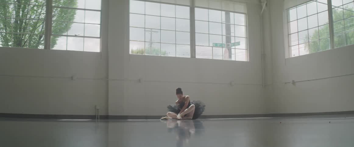 A white ballet dancer puts on her shoes while sitting on the floor