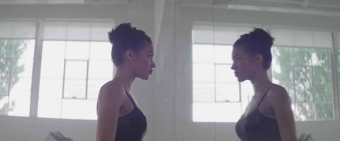 Ballet dancer in black costume looks in the mirror indoors during daylight