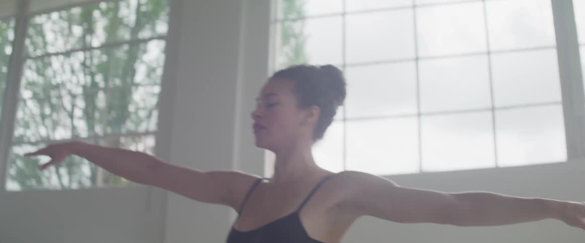 Ballet dancer wearing black ballet costume dances indoors during daylight