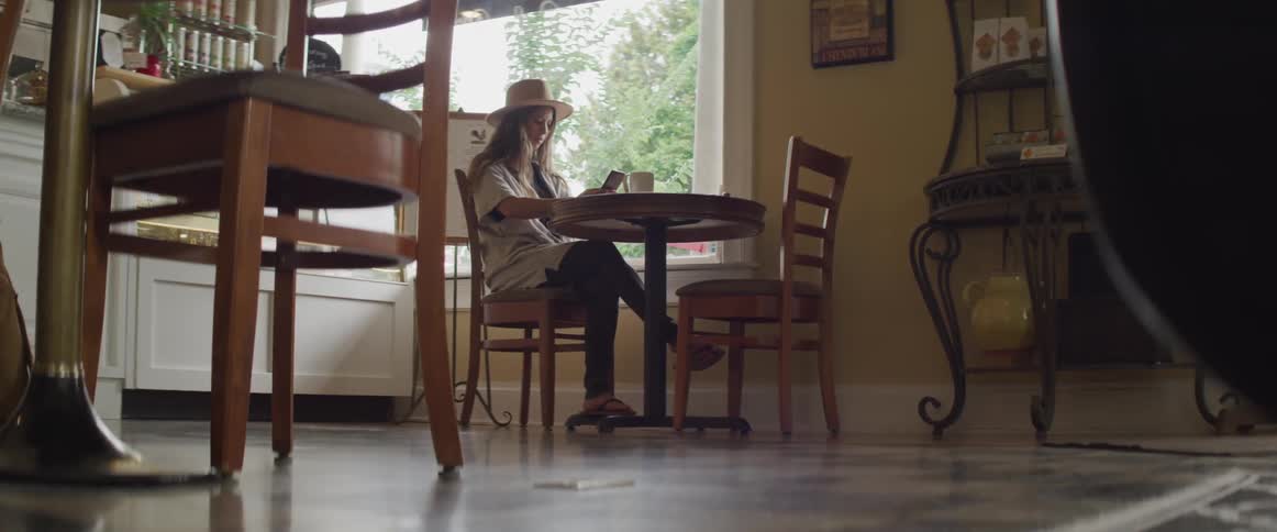 A woman sits at a table next to a window