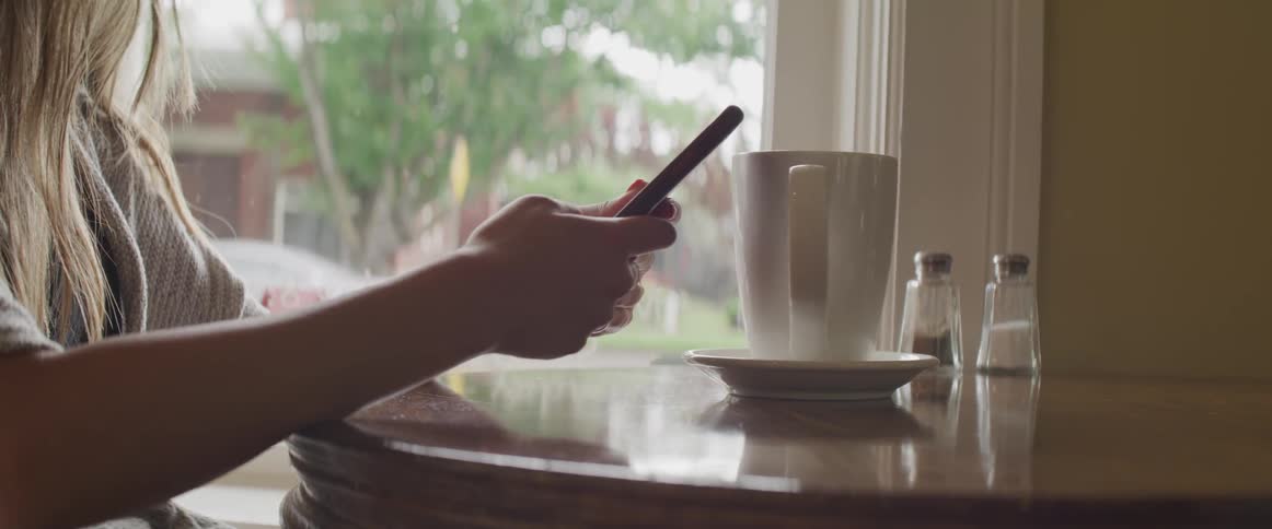 A woman is sitting at a table using her phone