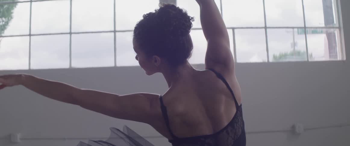 A ballerina in a dance studio dancing with a window in the background