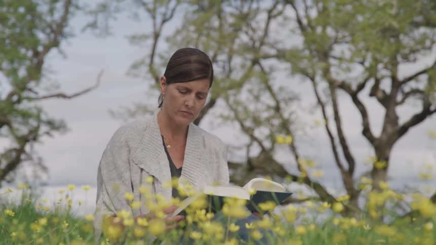 A woman reads a book while sitting in a field of flowers