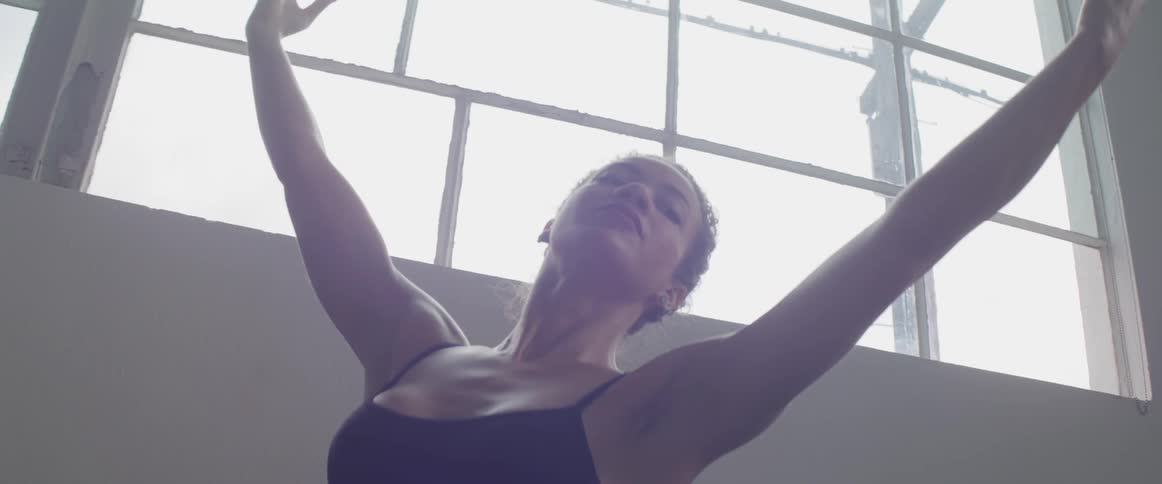 A young ballerina dressed in black performing in a white room near a large window