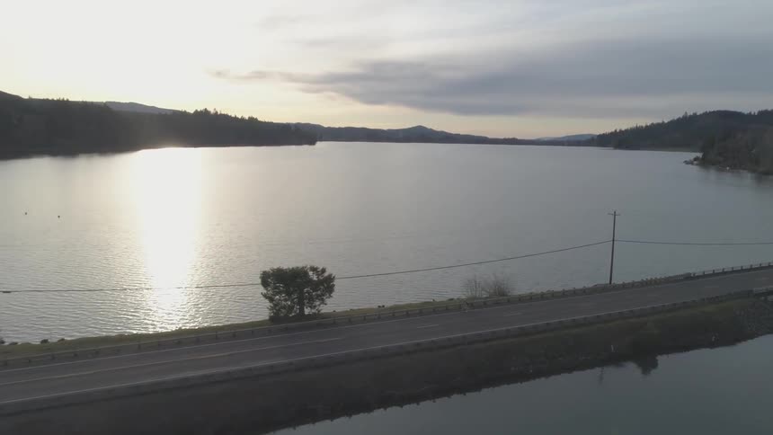 A person rides a bicycle onto a road that juts out onto the water at sunset