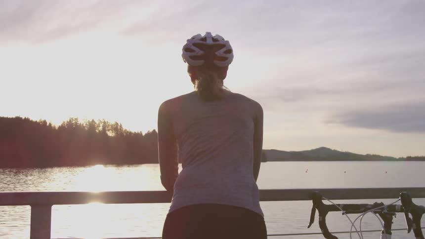 A bike rider leans over a fence staring at a lake