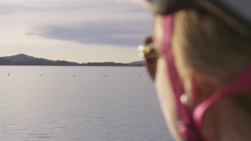 A woman wearing a helmet and sunglasses looks out at the water