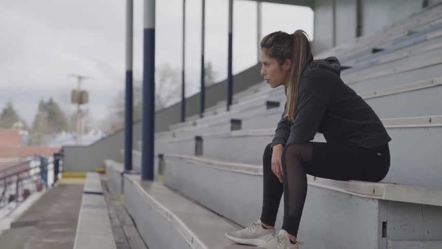 A woman sits on a bench in an empty section of bleachers