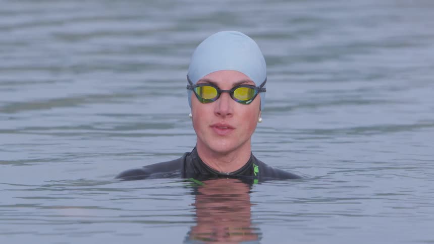 A woman in a swimming cap and goggles swims in a lake