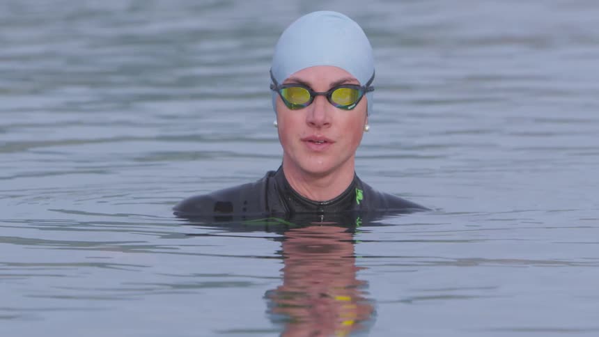 Woman wears goggles skin suit and swimming cap while partially submerged in water