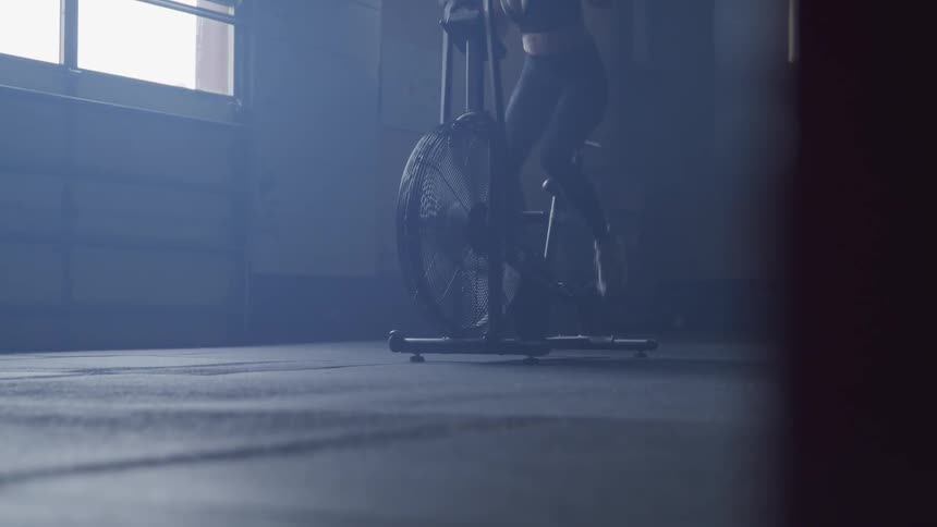 A woman rides an exercise bike in a shady room