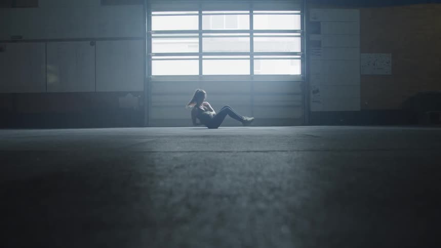 A woman sits on the floor and does russian twists with a medicine ball exercise