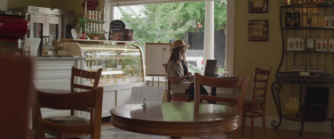 A woman is sitting in a cafe typing on a laptop