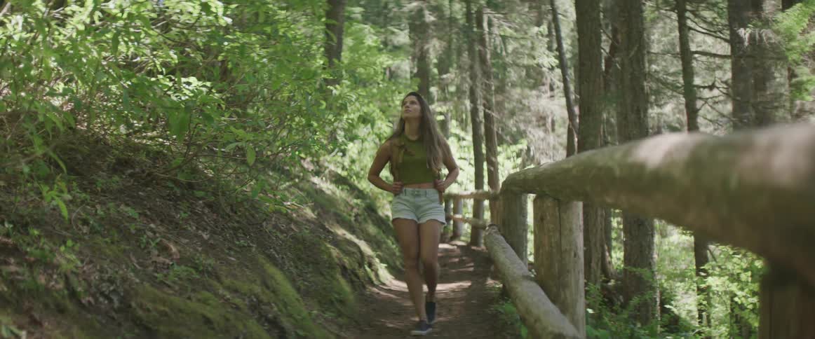 A woman in denim shorts walks through a forest path