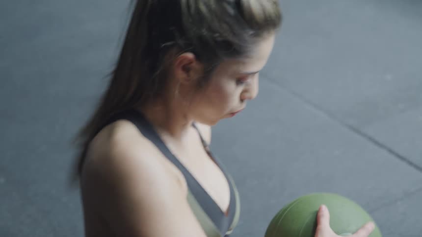 A woman with her hair pulled into a pony tail works out with a green medicine ball by twisting to her left and right