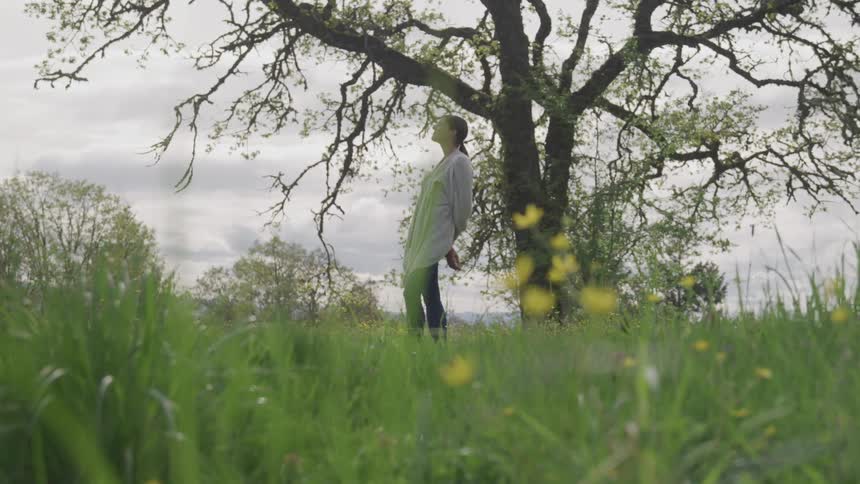 Woman stands on the grass under the tree on a cloudy day