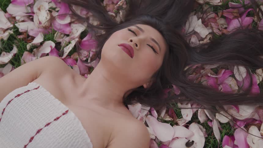 An asian woman lies on a bed of flower petals