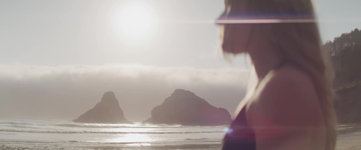Blonde woman stands on the white sand beach and looks at the ocean during daylight