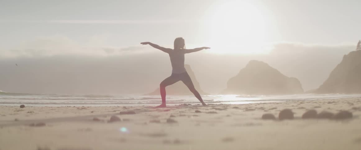 A white woman does yoga on a sandy beach