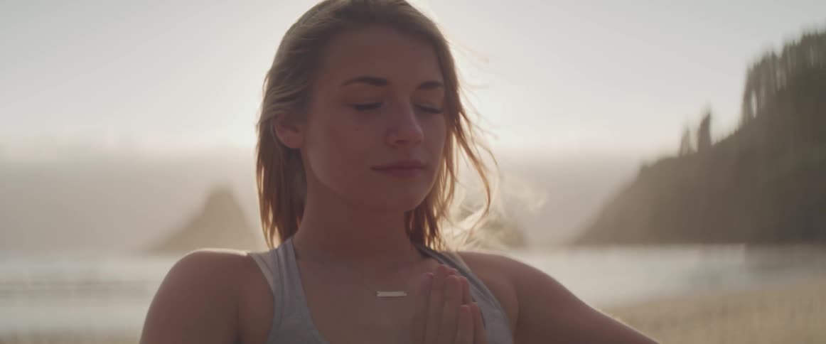 A woman close to the shore meditating with the sun in the background