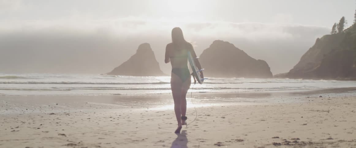A woman carrying a surfboard runs down the beach and into the ocean
