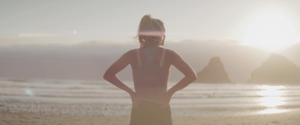A woman stands on the beach and looks out at the water