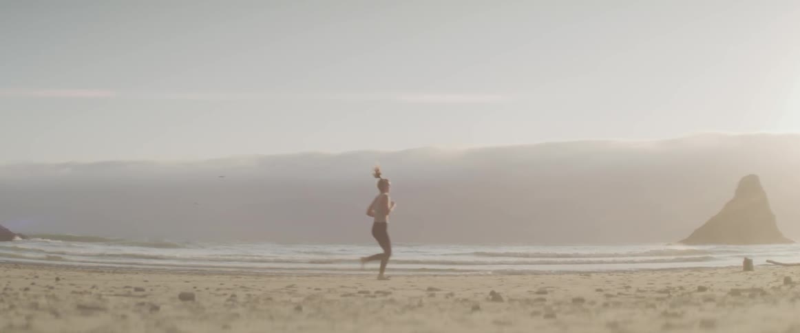 A woman in yoga pants and a sports bra jogs on a sandy beach at sunset