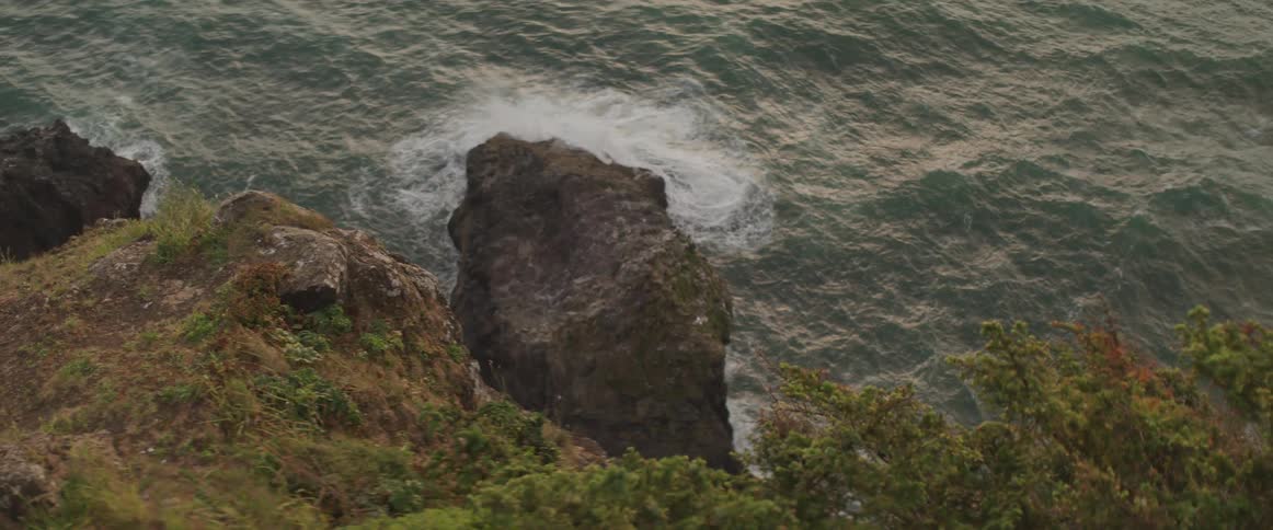 Waves crash into rocks below a cliff