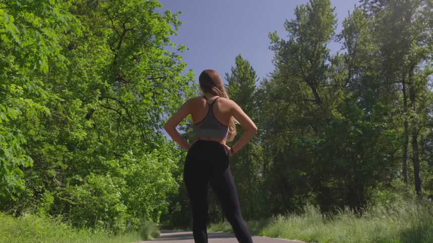 Woman stands with arms akimbo on the asphalt road in the forest during daylight