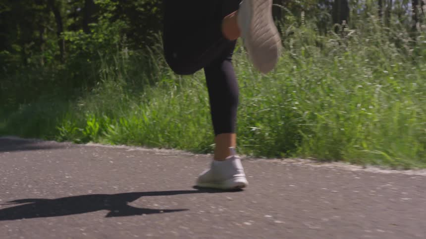A female is taking long strides running on a road through a forested area
