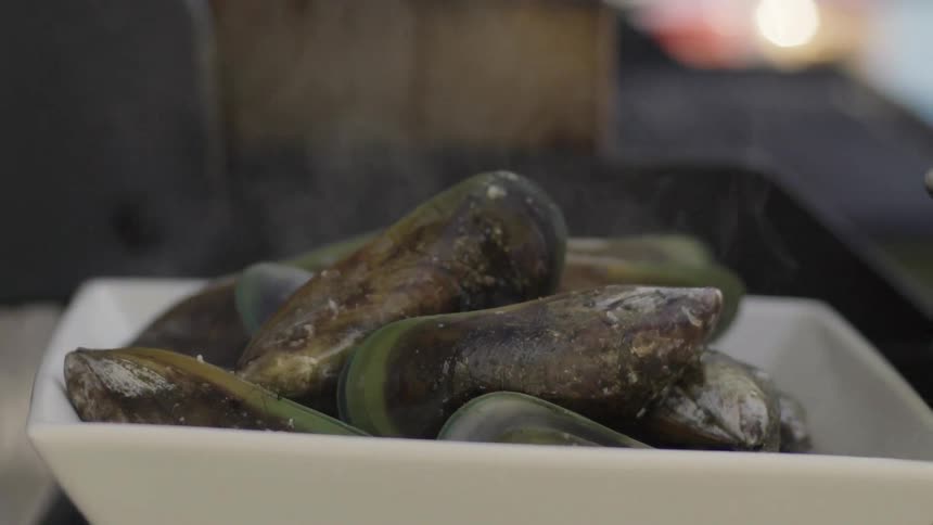 A person using tongs to place steaming clams in a bowl