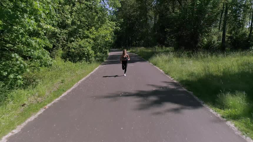 A woman is jogging on a road in a forest area