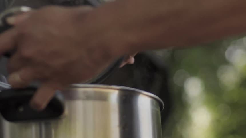 A person is stirring food in a large silver pot