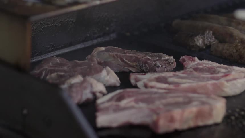 Someone Grilling Steaks Outdoors Over Open Flame During Relaxed Barbecue Gathering.