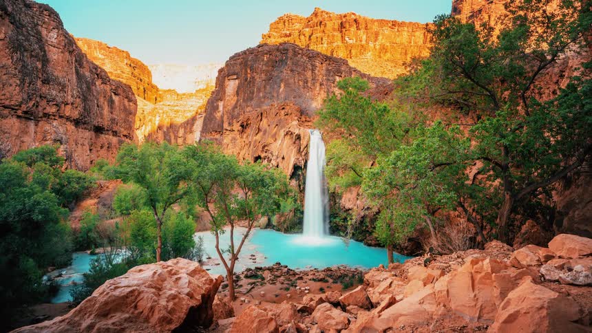 A waterfall flows through the rocks into a lake surrounded by mountains