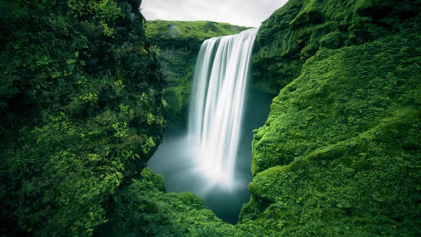 A waterfall flowing over a moss covered canyon
