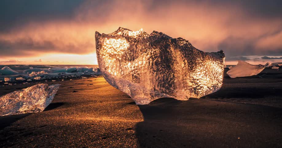 A view of ice chunks on top of the sandy shore reflecting the red night sky
