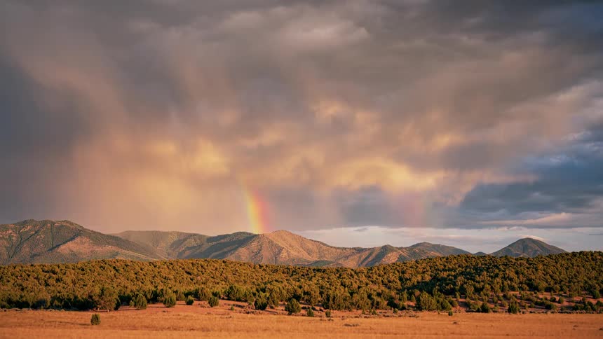 A view of a mountain range and the moving sky over a rainbow