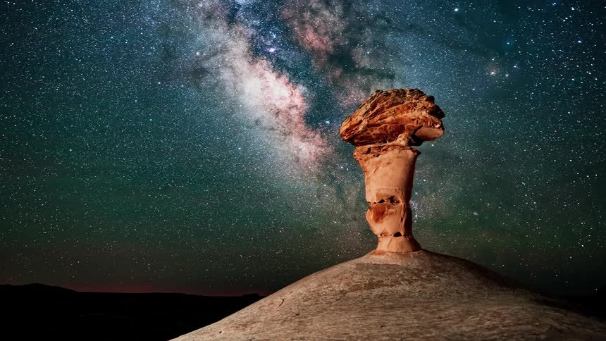 A large rock formation with the milky way moving across the night sky
