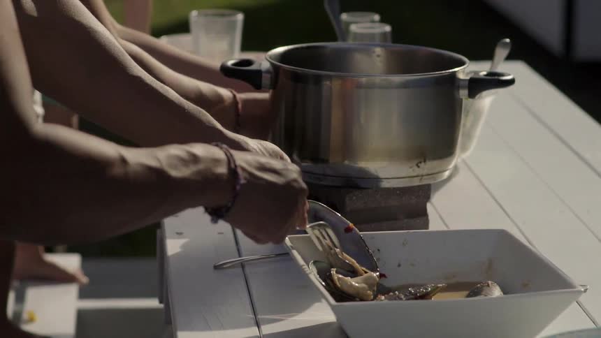 People Cooking Food Together Outdoors Around Grill in Warm Natural Daylight Setting.